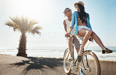 Buy stock photo Shot of a young couple riding a bicycle together on the promenade