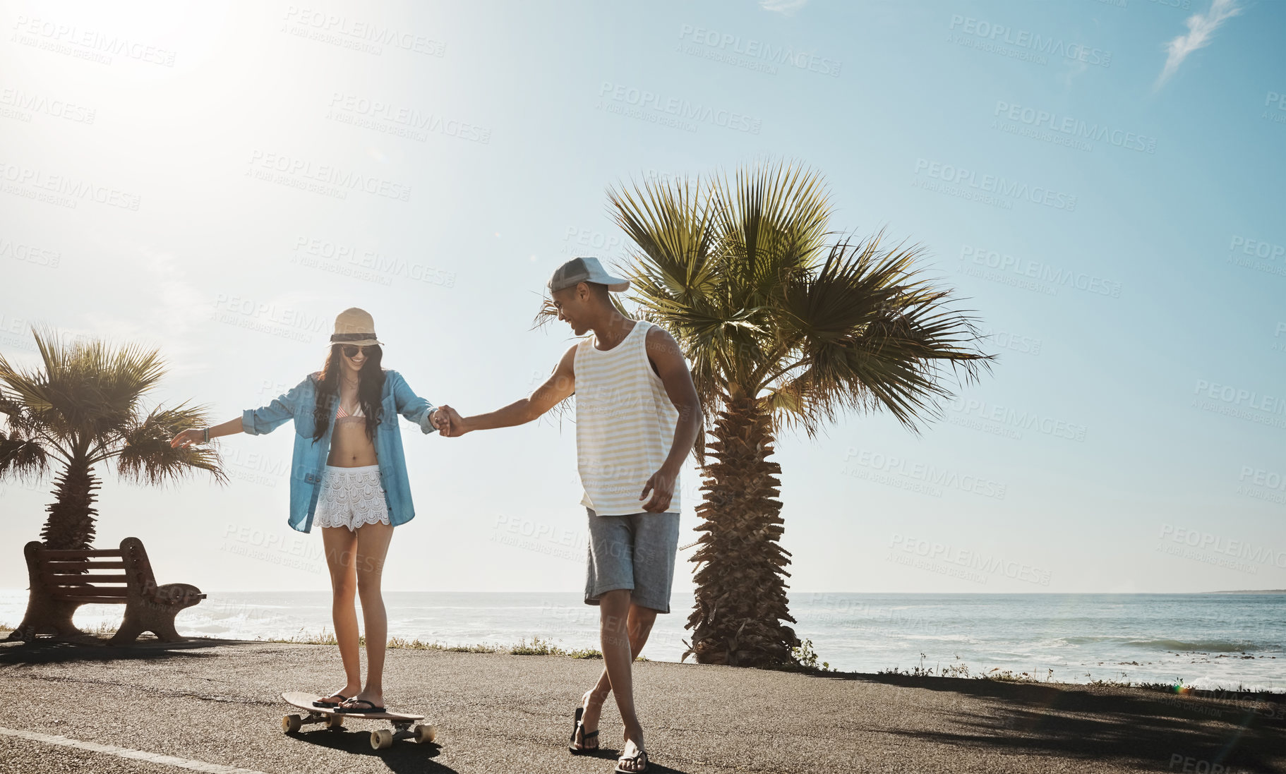 Buy stock photo Shot of a young man teaching his girlfriend how to skateboard on the promenade