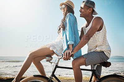 Buy stock photo Shot of a young couple riding a bicycle together on the promenade