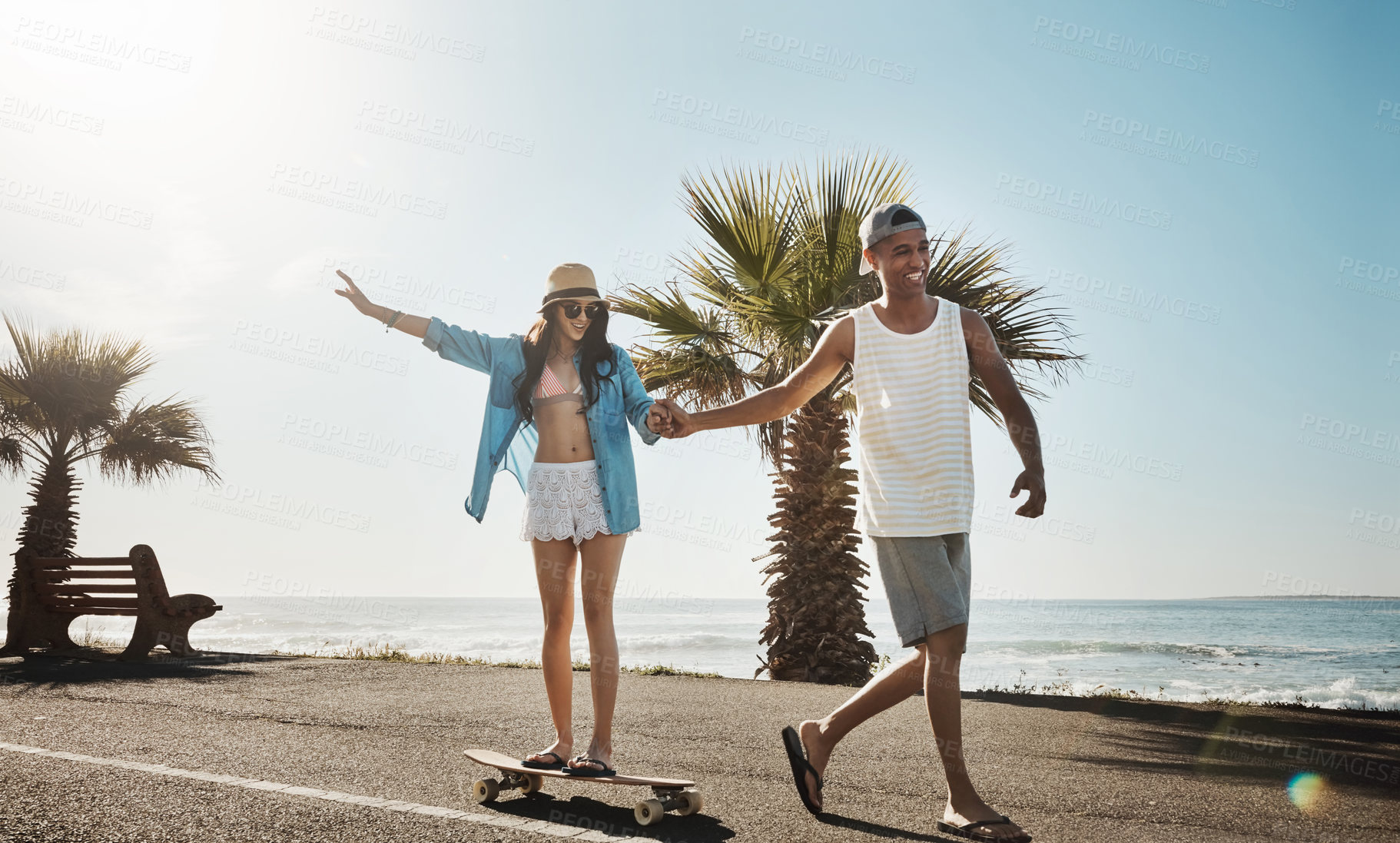 Buy stock photo Shot of a young man teaching his girlfriend how to skateboard on the promenade