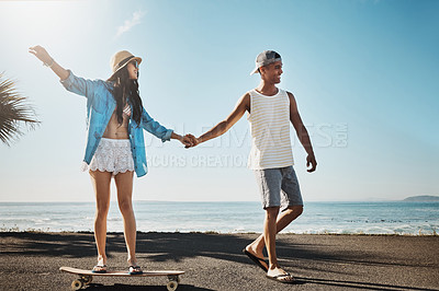 Buy stock photo Shot of a young man teaching his girlfriend how to skateboard on the promenade