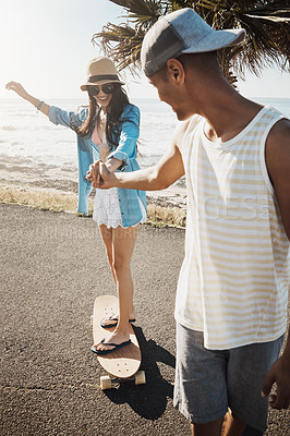 Buy stock photo Shot of a young man teaching his girlfriend how to skateboard on the promenade