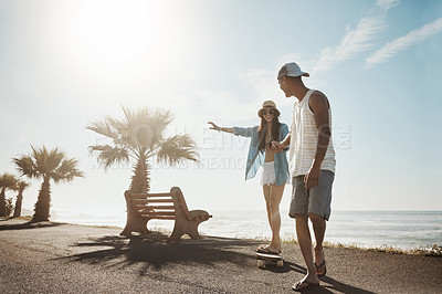 Buy stock photo Shot of a young man teaching his girlfriend how to skateboard on the promenade