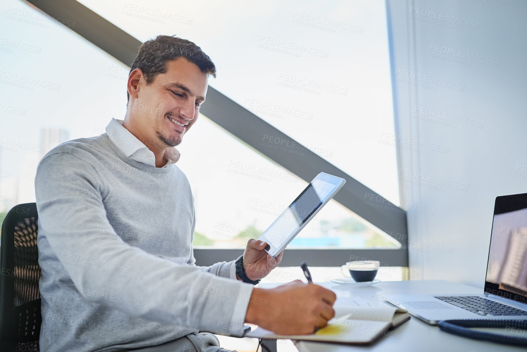 Buy stock photo Shot of a young businessman writing notes while working on a digital tablet in an office