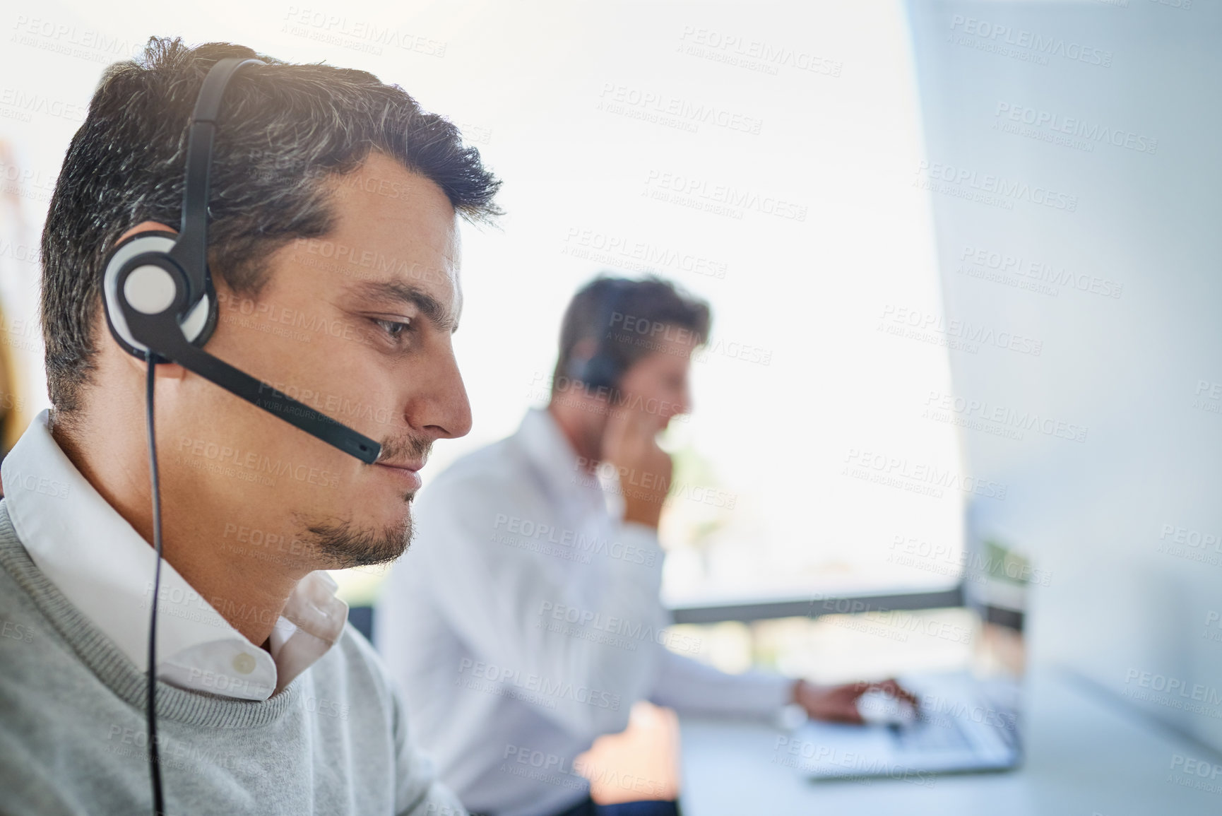 Buy stock photo Shot of a young call centre agent working in an office with his colleagues in the background