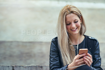 Buy stock photo Shot of an attractive woman using a mobile phone and earphones in the city