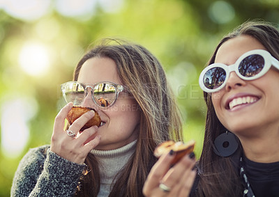 Buy stock photo Cropped shot of two attractive young women eating a peach while sitting in the park