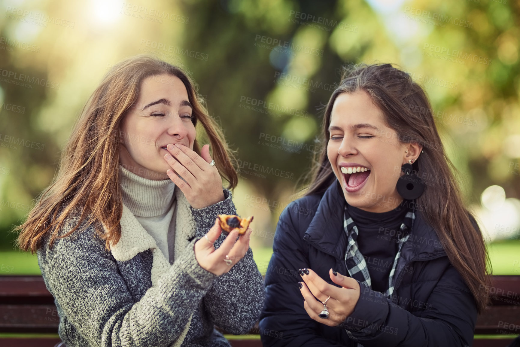 Buy stock photo Cropped shot of two attractive young women eating a peach while sitting in the park