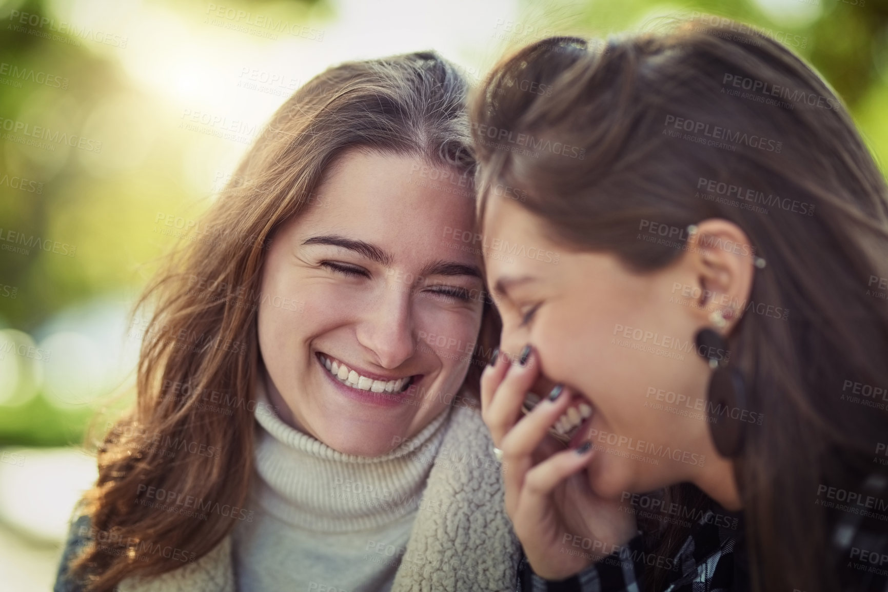 Buy stock photo Cropped shot of two attractive young women laughing while sitting in the park