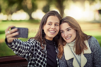 Buy stock photo Cropped shot of two attractive young women taking selfies while sitting in the park