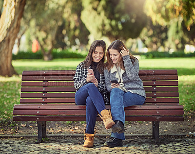 Buy stock photo Full length shot of two attractive young women using their cellphones while sitting in the park