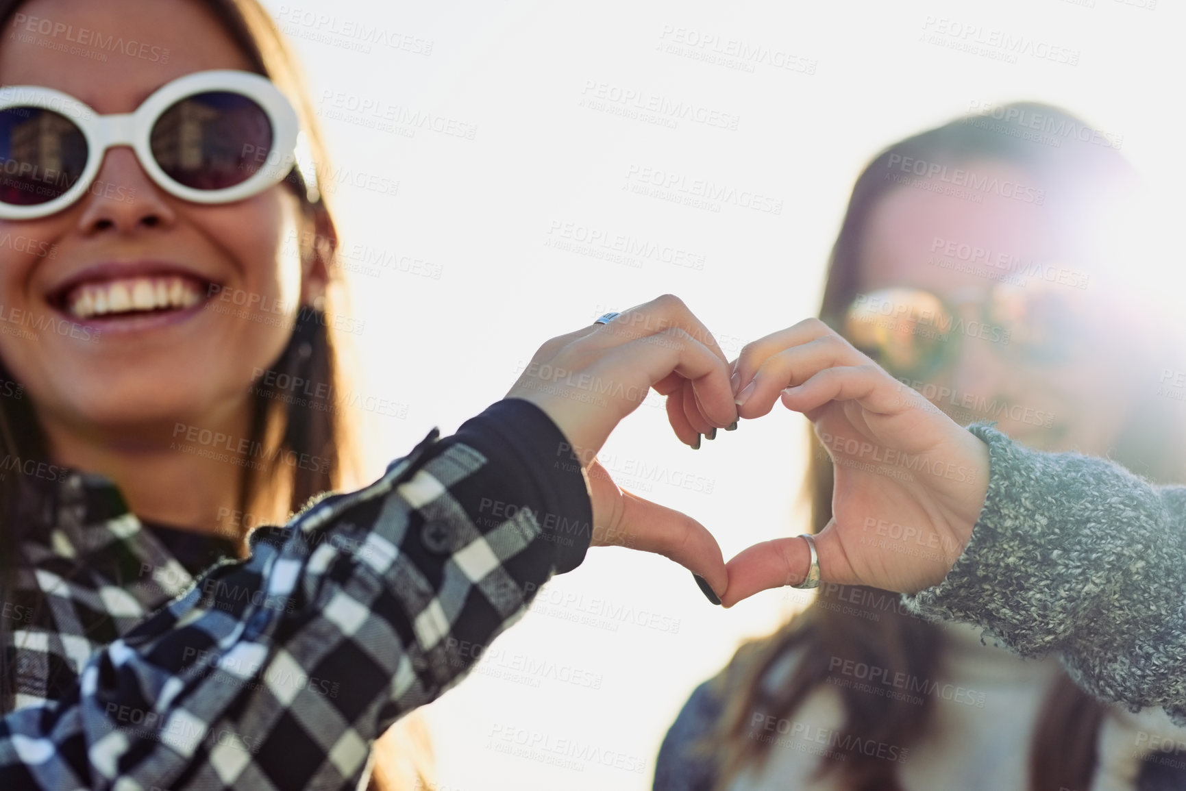 Buy stock photo Cropped portrait of two attractive young women making a heart shape with their hands while outdoors