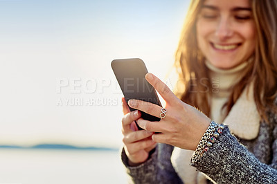 Buy stock photo Cropped shot of an attractive young woman using her cellphone while out by the ocean