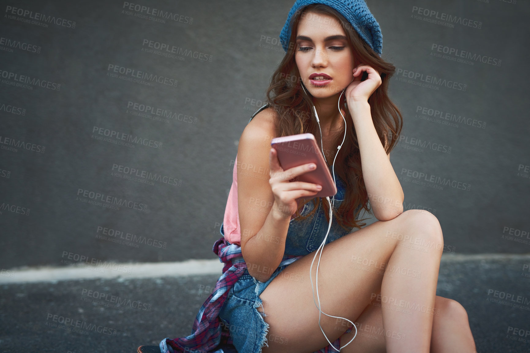 Buy stock photo Shot of a carefree young woman seated on the floor while listening to music through her earphones outside during the day