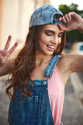 Buy stock photo Shot of an attractive young woman posing with a cap on and showing the peace sign outside during the day