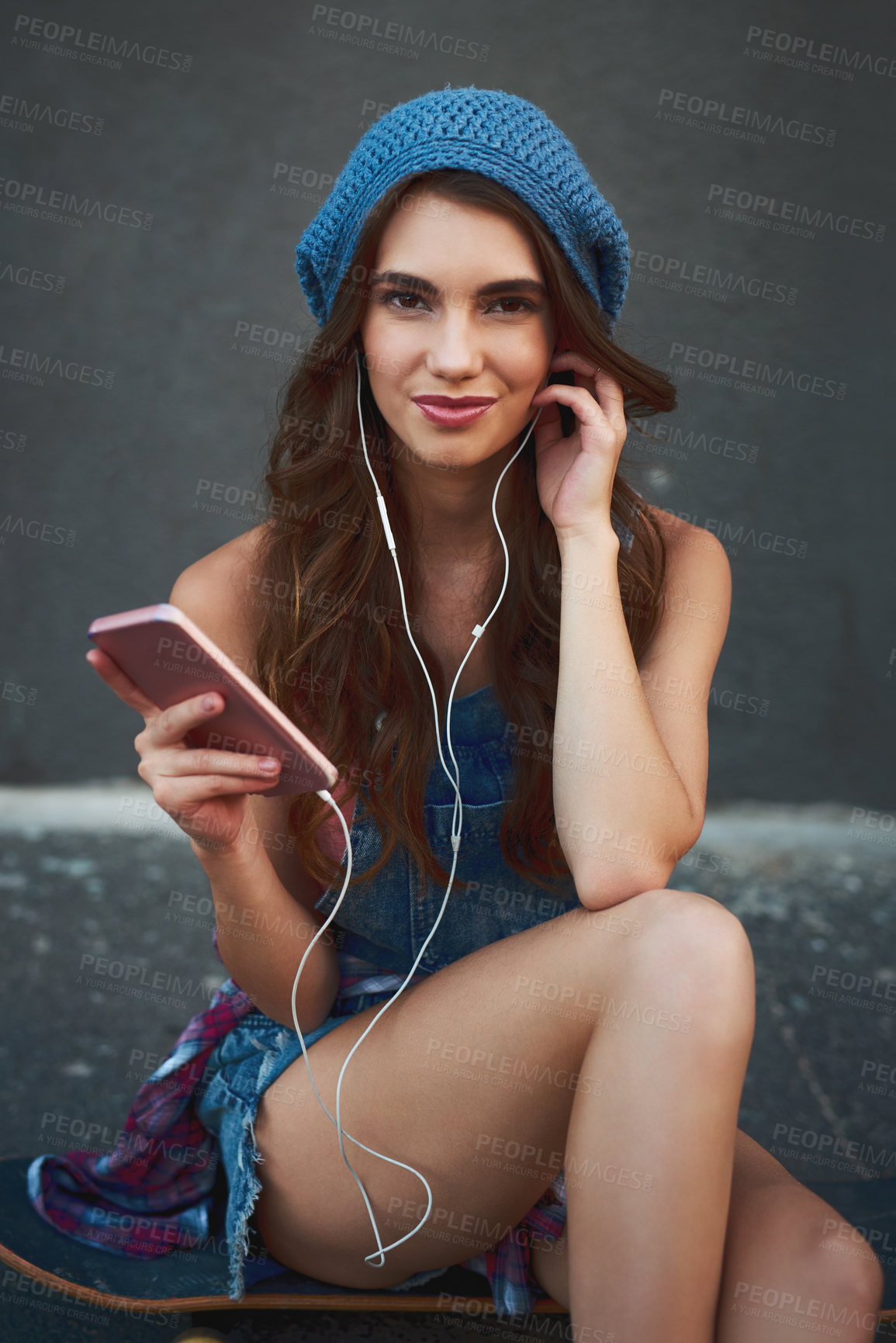 Buy stock photo Portrait of a carefree young woman seated on the floor while listening to music through her earphones outside during the day
