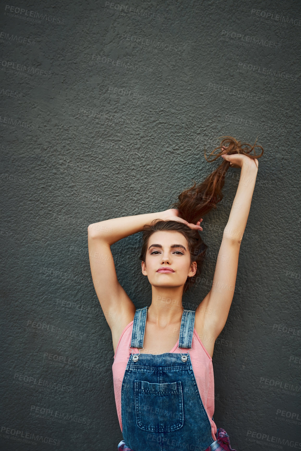 Buy stock photo Portrait of a carefree young woman holding her hair up while standing against a grey background