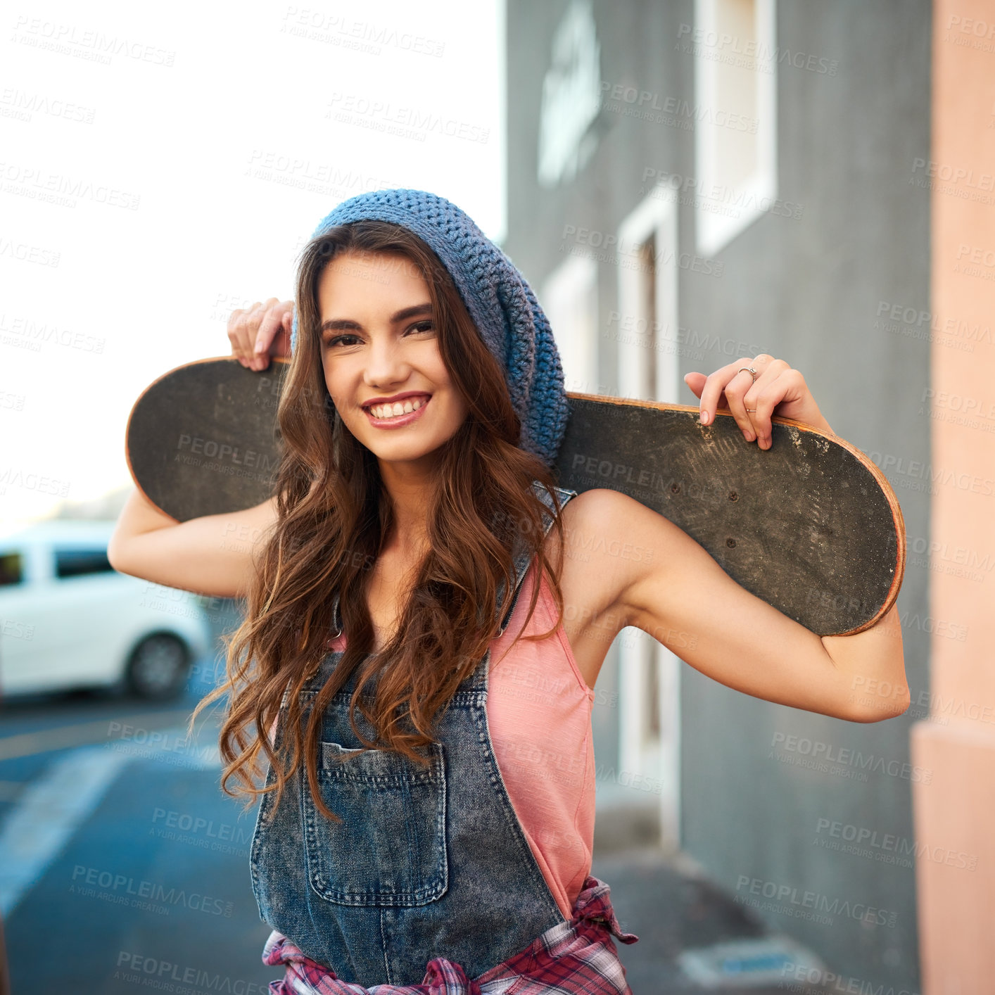 Buy stock photo Portrait of an attractive young female skater holding a skateboard behind her back outside during the day