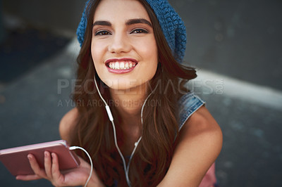 Buy stock photo Portrait of a carefree young woman seated on the floor while listening to music through her earphones outside during the day