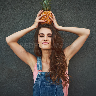 Buy stock photo Portrait of a cheerful young woman holding a pineapple on her head while standing against a grey background