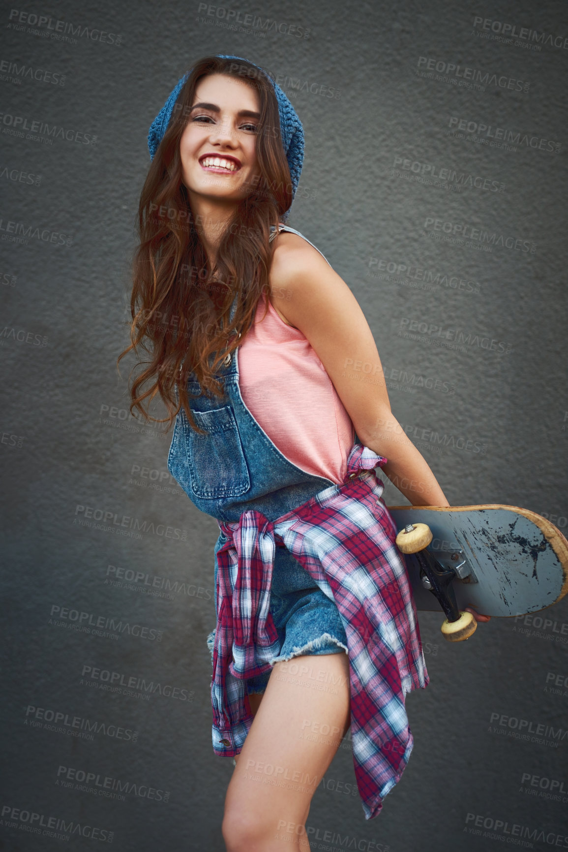 Buy stock photo Shot of an attractive young female skater holding a skateboard behind her back while standing against a grey background