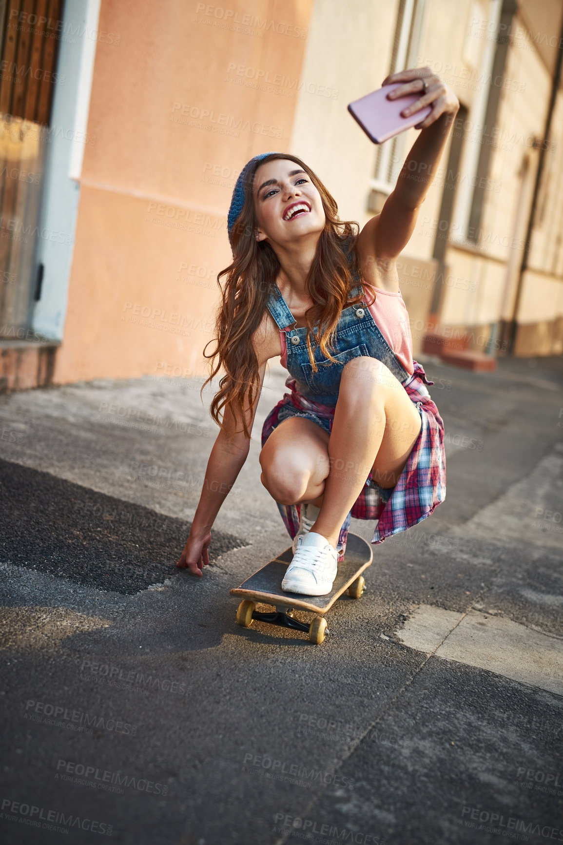 Buy stock photo Shot of a carefree young woman riding low on a skateboard while taking a self portrait with her cellphone outside during the day