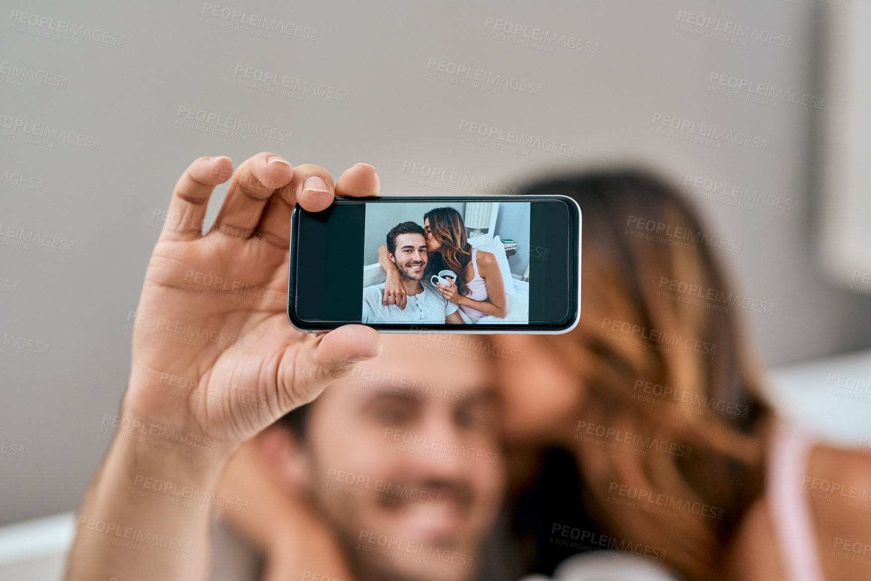 Buy stock photo Phone screen, selfie and smile of couple in bedroom of hotel in celebration of anniversary or honeymoon. Kiss, love or romance with happy man and woman on bed in morning for bonding or wellness