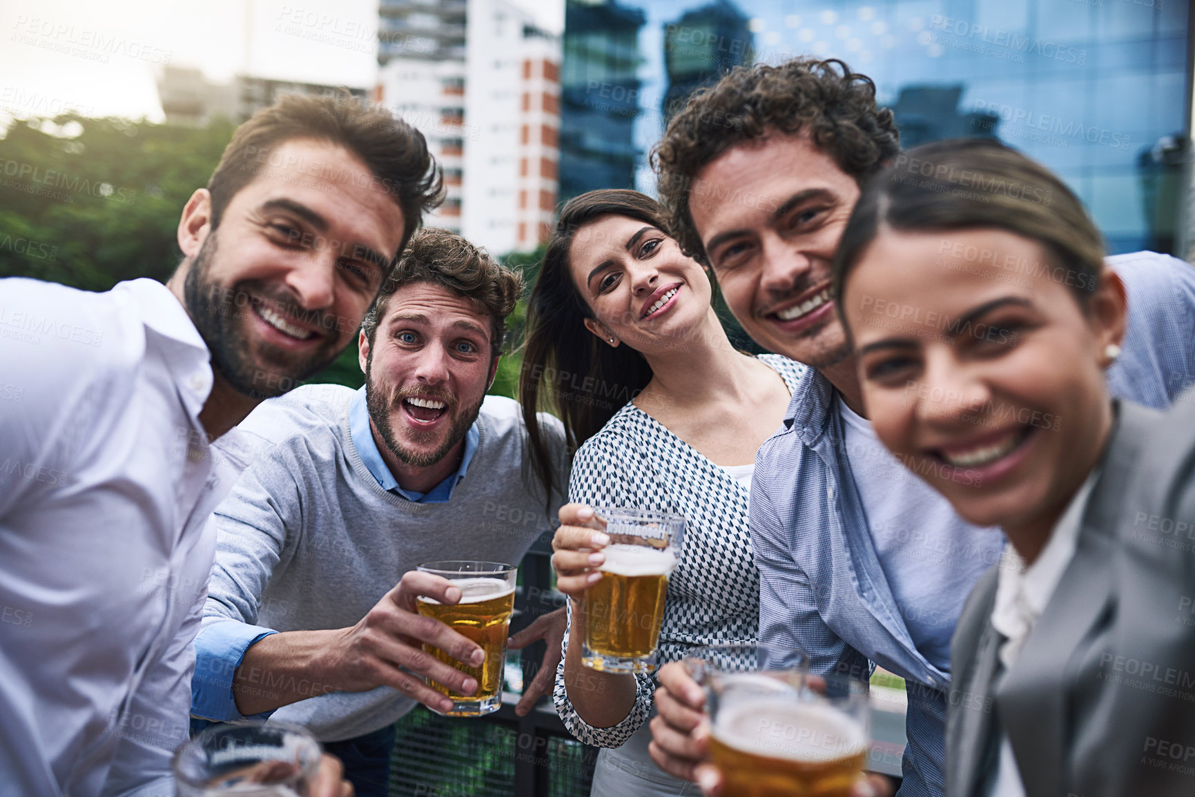 Buy stock photo Portrait of a cheerful group of young work colleagues getting close for a photo together while drinking beer outside during the day