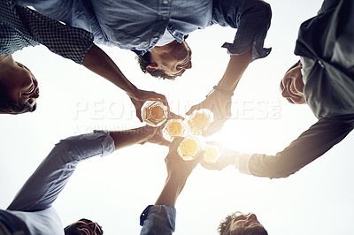 Buy stock photo Low angle shot of a group of cheerful young work colleagues forming a huddle and having a celebratory toast with beer outside during the day