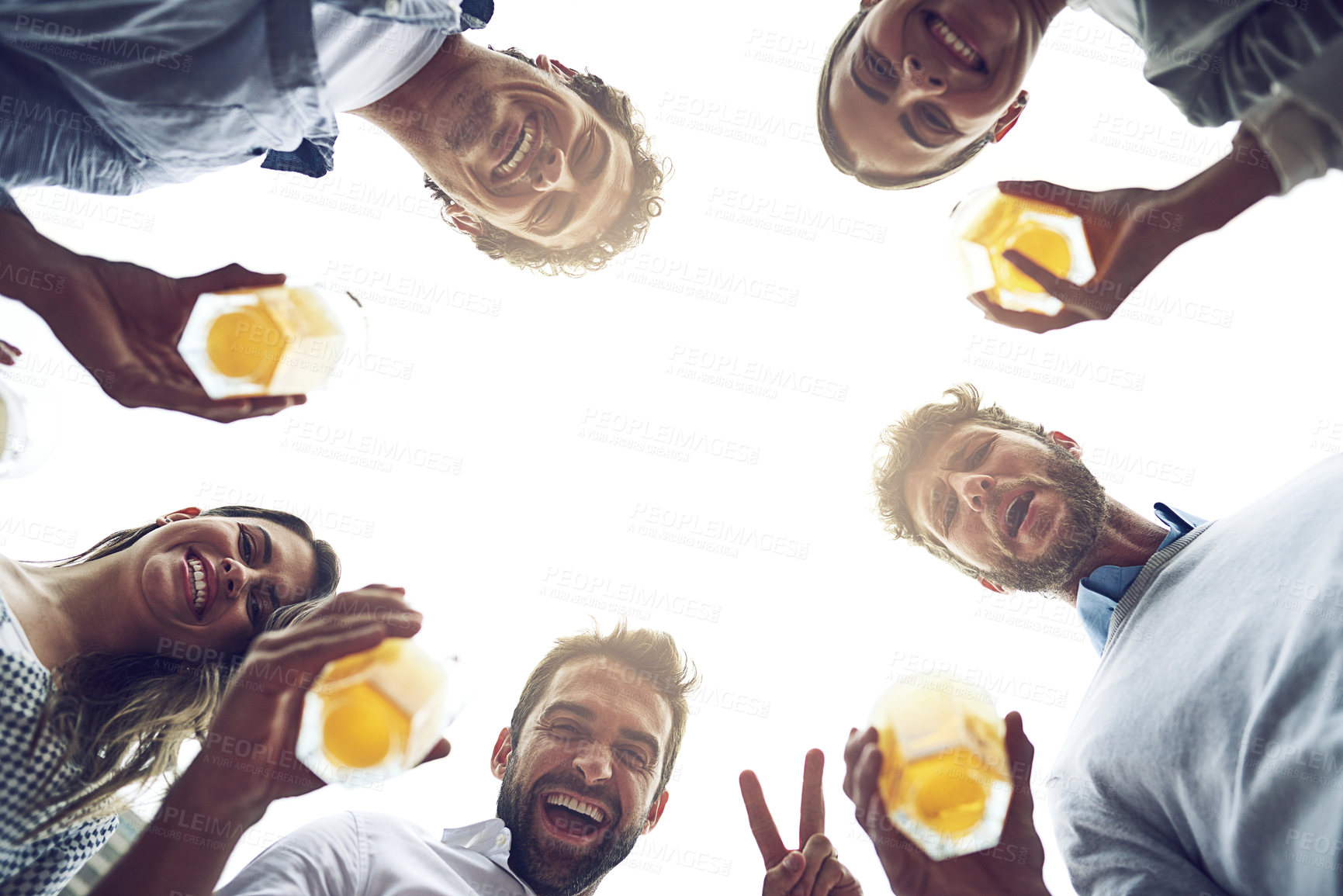 Buy stock photo Low angle portrait of a group of cheerful young work colleagues standing in a circle while drinking beer together outside during the day