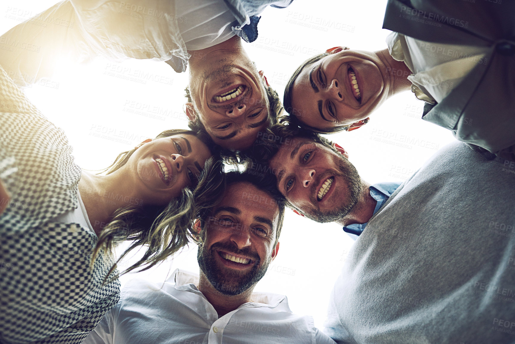 Buy stock photo Low angle portrait of a group of cheerful young work colleagues standing in a circle and looking down outside during the day