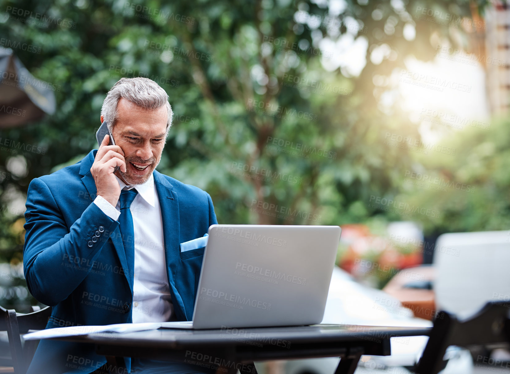 Buy stock photo Shot of a handsome mature businessman in corporate attire on a call and using a laptop outside during the day