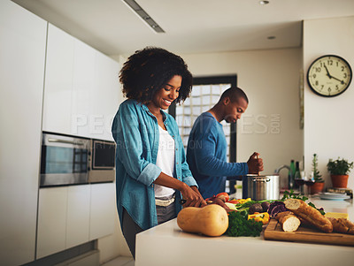 Buy stock photo Shot of a cheerful young couple preparing food together in the kitchen at home during the day