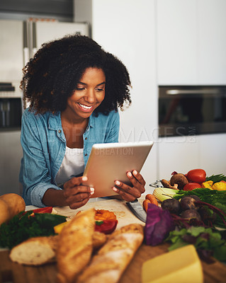 Buy stock photo Shot of a cheerful young woman browsing on a digital tablet while being surrounded by vegetables in the kitchen at home during the day