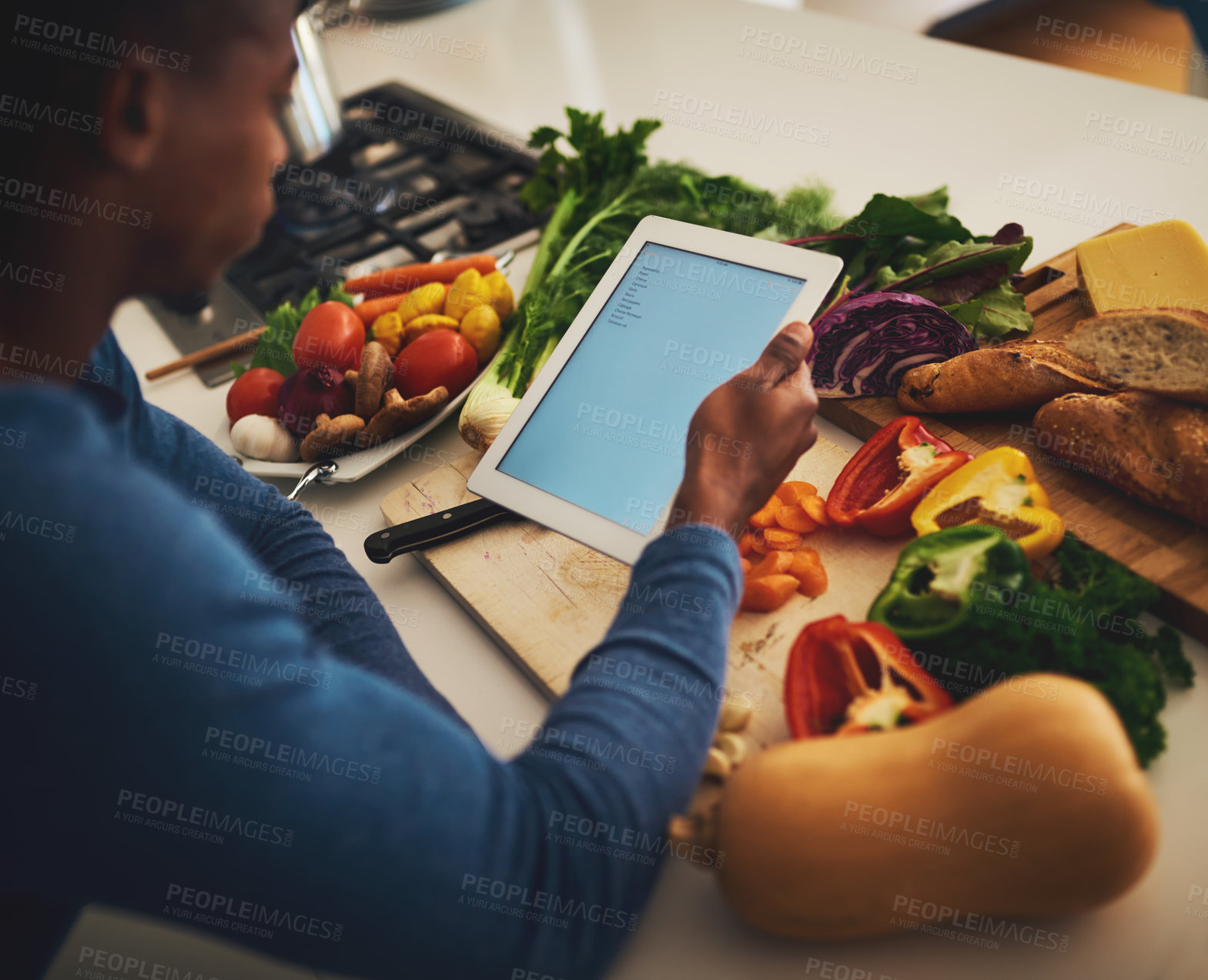Buy stock photo Shot of a focused young man holding a digital tablet over a bunch of vegetables in the kitchen at home