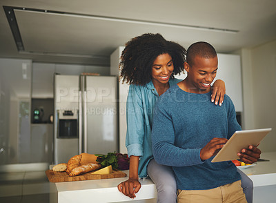 Buy stock photo Shot of a cheerful young couple relaxing in the kitchen while browsing on a digital tablet at home during the day