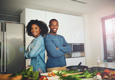 Buy stock photo Portrait of a cheerful young couple standing together over a table full of ingredients that they're about to use for cooking in the kitchen at home