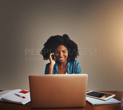 Buy stock photo Studio shot of an attractive young woman talking on a cellphone while working on a laptop against a dark background