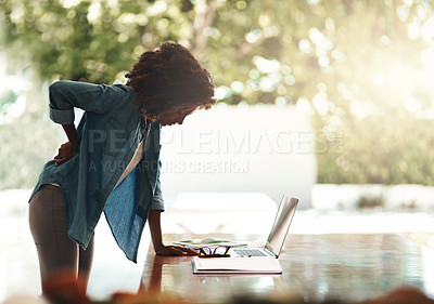 Buy stock photo Shot of a young woman holding her back in pain while getting up from her desk at home
