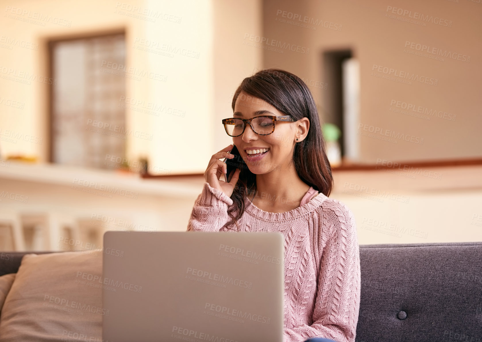 Buy stock photo Shot of an attractive young woman using a laptop and phone on the sofa at home