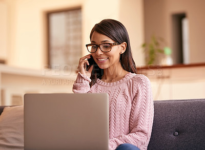 Buy stock photo Shot of an attractive young woman using a laptop and phone on the sofa at home