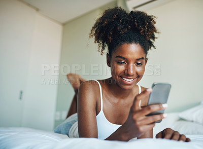 Buy stock photo African woman, happy and texting with mobile phone for relax, calm and peace in cozy or comfort in home. Female person, smile and morning for wake up in bedroom on tech for health, wellness and rest