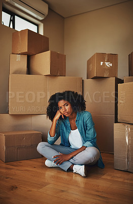Buy stock photo Portrait of a unhappy looking young woman seated on the ground while being surrounded by cardboard boxes on moving day inside at home
