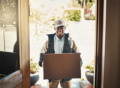 Buy stock photo Portrait of a cheerful young deliveryman holding a box while standing in a doorway at a house during the day