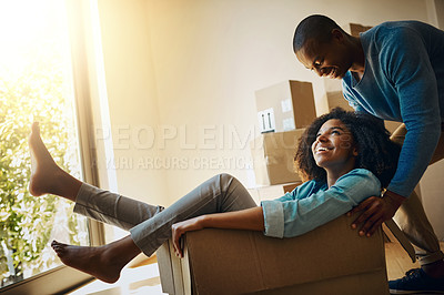 Buy stock photo Shot of a cheerful young man pushing his girlfriend around in a cardboard box at home during moving day
