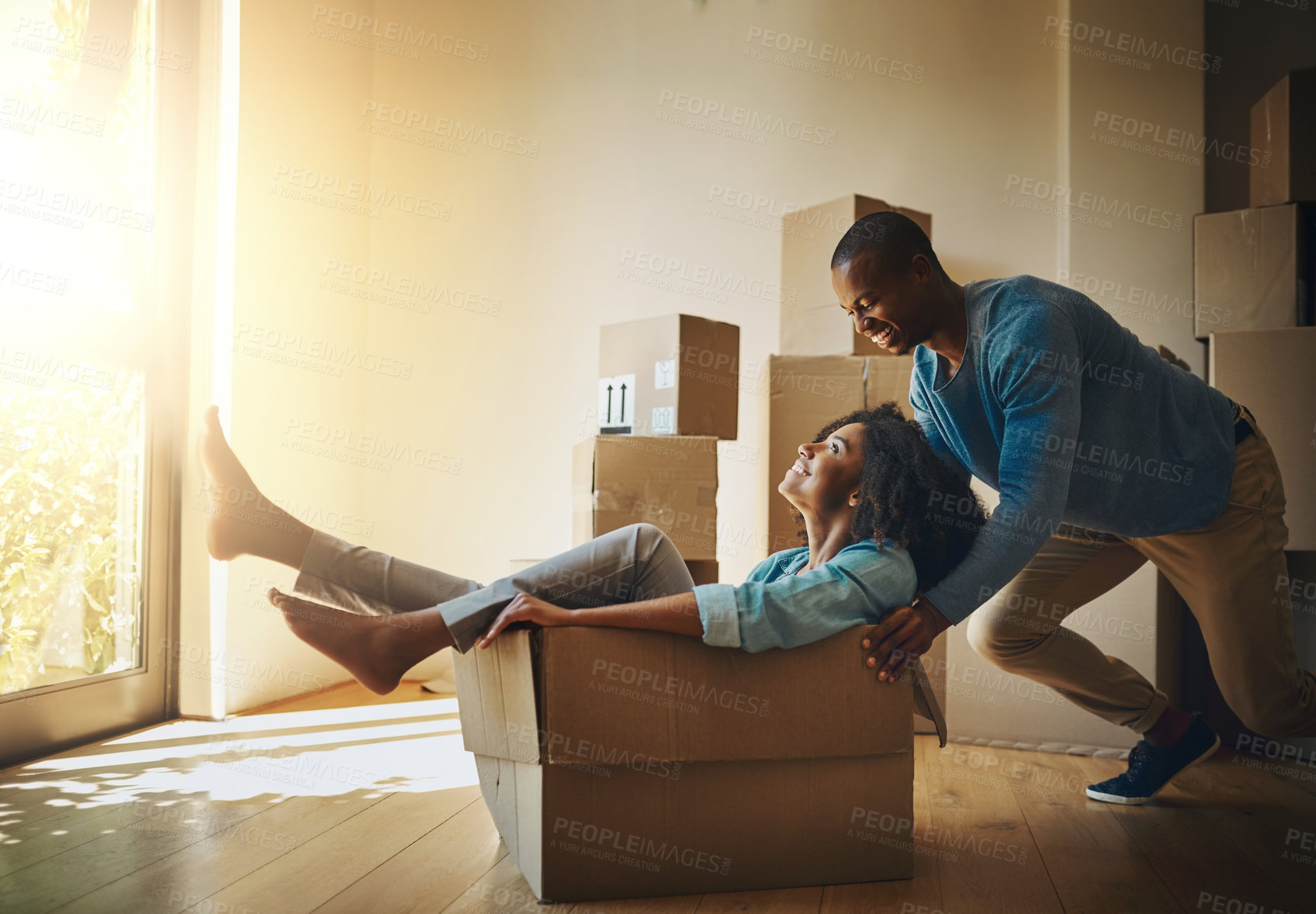 Buy stock photo Shot of a cheerful young man pushing his girlfriend around in a cardboard box at home during moving day