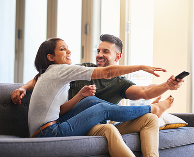 Buy stock photo Shot of a young couple fighting over the remote control while watching tv at home