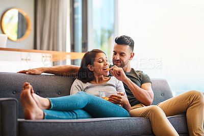 Buy stock photo Love, happy couple on sofa and eating chips in living room of their home. Caring or bonding together, relaxing or comfortable and happy married people on couch watching television for quality time.