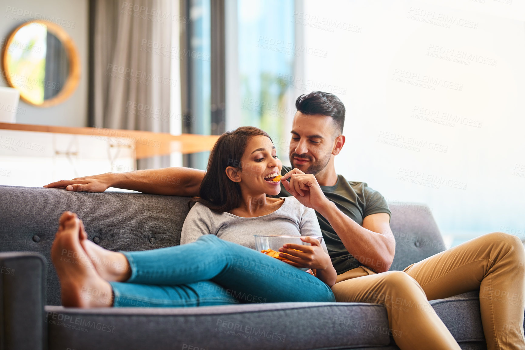 Buy stock photo Love, happy couple on sofa and eating chips in living room of their home. Caring or bonding together, relaxing or comfortable and happy married people on couch watching television for quality time.