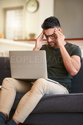 Buy stock photo Shot of a handsome young man suffering with a headache while working on a laptop at home